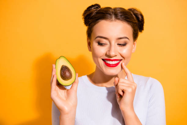 close up foto bonita ela sua senhora bonita penteado segurar fatia abacate olhar lado com interesse mão braço dedo queixo gostoso saboroso desgaste casual branco pullover roupa isolado fundo amarelo - women eating fruit food - fotografias e filmes do acervo