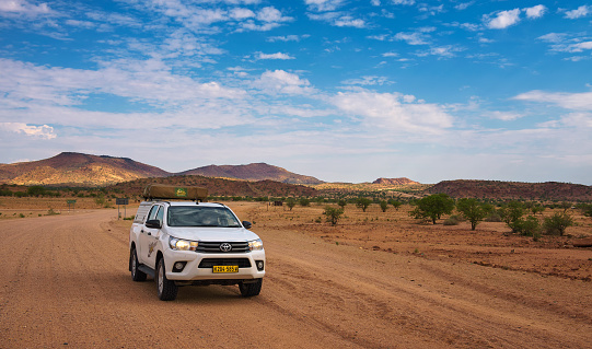 Damaraland, Namibia - March 30, 2019: Typical 4x4 rental car in Namibia equipped with camping gear and a roof tent driving on a dirt road through Damaraland.