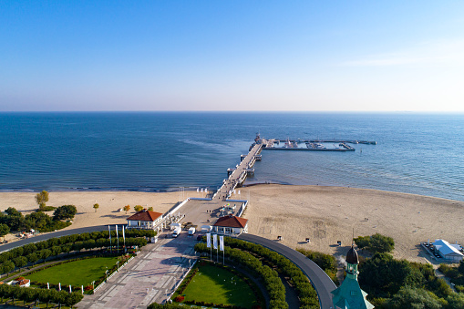 Sopot resort in Poland. Wooden pier (molo) with marina, yachts, beach, old lighthouse, walking people, vacation infrastructure, park and promenade. Aerial view at sunrise.