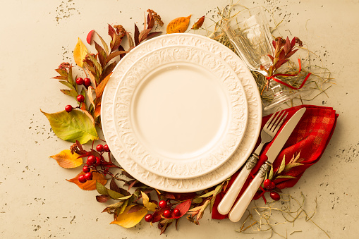 Autumn (fall) or thanksgiving table setting design captured from above (top view, flat lay). Empty white plate, glass, cutlery and decorations (colorful leaves). Background with free text space.
