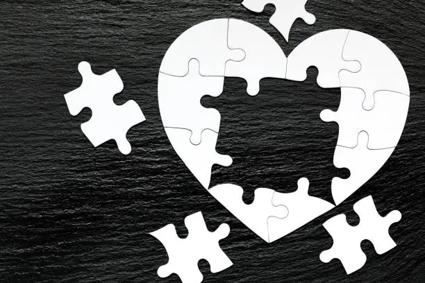 Heart-shaped jigsaw puzzle on color background. Puzzle heart on wooden background. A missing piece of the heart puzzle. Heart shape jigsaw puzzle. Puzzles in the shape of a heart.