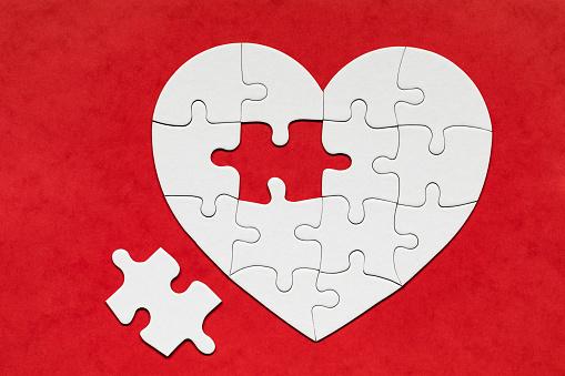 Heart-shaped jigsaw puzzle on color background. Puzzle heart on wooden background. A missing piece of the heart puzzle. Heart shape jigsaw puzzle. Puzzles in the shape of a heart.