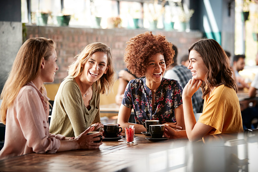Cuatro jóvenes amigas reunión sentarse a la mesa en la cafetería y hablar photo