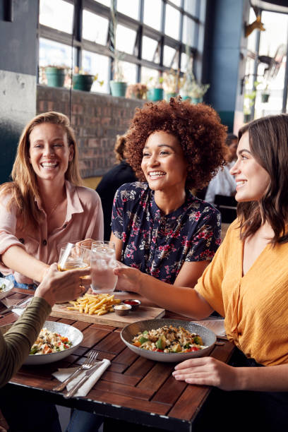 cuatro jóvenes amigas reunión para bebidas y comida haciendo un brindis en el restaurante - restaurant food dinner lunch fotografías e imágenes de stock