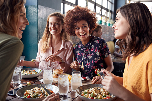 Cuatro jóvenes amigas reunión para bebidas y comida haciendo un brindis en el restaurante photo
