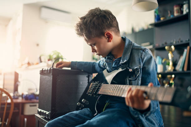 Little boy playing electric guitar Little boy playing electric guitar in the living room. The boy is sitting on the table and is tuning the amplifier. 
Nikon D850 amplifier photos stock pictures, royalty-free photos & images