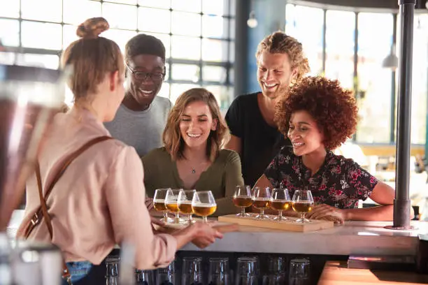Photo of Waitress Serving Group Of Friends Beer Tasting In Bar
