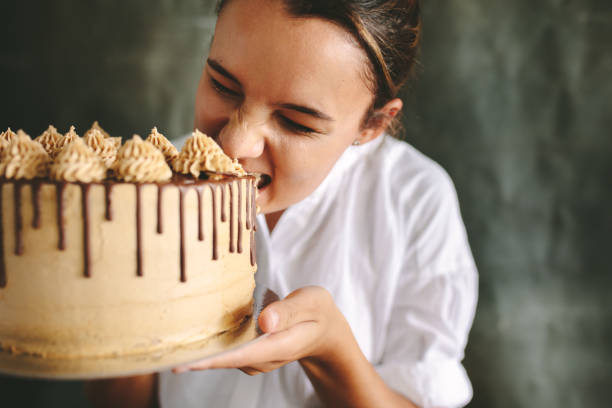 Bakery sweet food and people concept. Content attractive woman closed eyes holds cake cupcake in hand smelling orange background