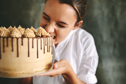 Female chef eating whole cake. Chef holding a big cake in hand and taking a bite.