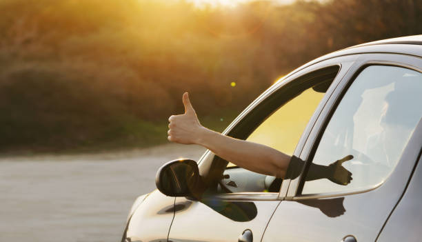 uomo che mostra i pollici in su dal finestrino dell'auto al tramonto - driving a car foto e immagini stock