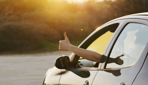 man showing thumbs up from car window at sunset - conduzir imagens e fotografias de stock
