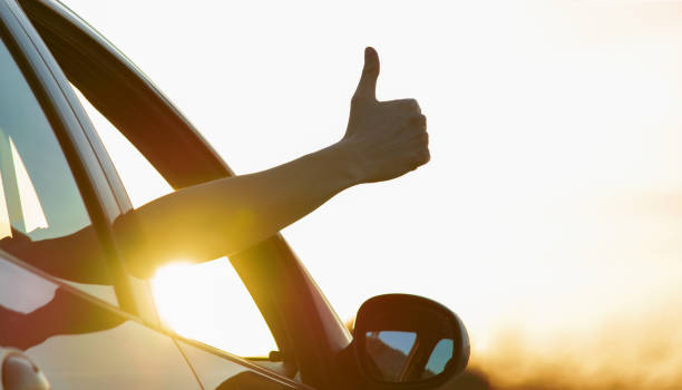 istock Man showing thumbs up from car window with sunset sky at background. 1146681208