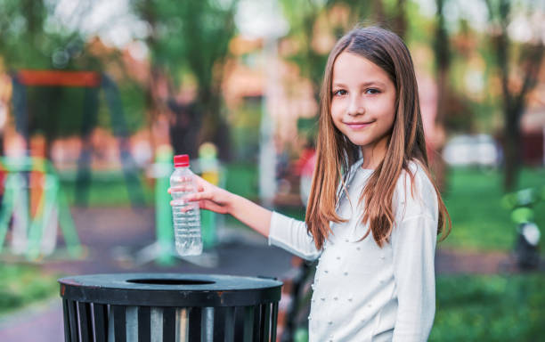 Little girl throwing bottle into the trash. Ecology concept stock photo