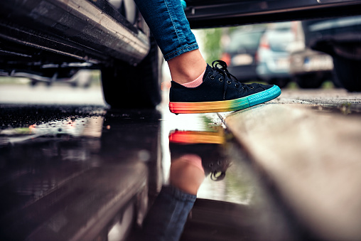 Girl wearing black sneakers stepping out of the car and avoiding puddle