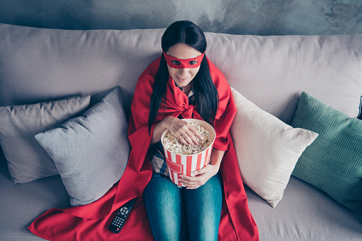 High angle top above photo beautiful she her superpower lady costume hold popcorn container watch premiere new long wait comics picture wear red eye mask mantle sit sofa couch divan house indoors.