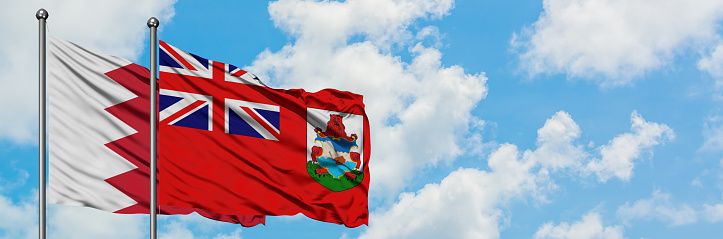Bahrain and Bermuda flag waving in the wind against white cloudy blue sky together. Diplomacy concept, international relations.