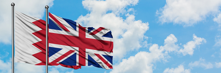 Bahrain and United Kingdom flag waving in the wind against white cloudy blue sky together. Diplomacy concept, international relations.