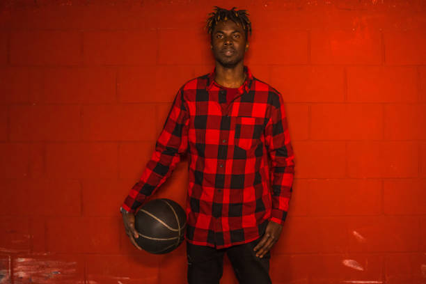 Cool man holding basketball Cool young man holding a basketball by a vivid red wall. He is wearing a red plaid shirt. long sleeved recreational pursuit horizontal looking at camera stock pictures, royalty-free photos & images