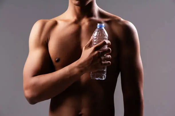 Photo of In selective focus of water bottle was holding by human hand,in front of fit and firm of body