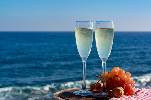Champagne, prosecco or cava served with pink grape in two glasses on outside terrace with sea view close up