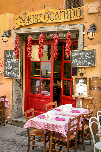 Rome, Italy, Feb 10 - A typical small restaurant with characteristic outdoor tables in the ancient Trastevere district, the most loved and visited roman district by the tourists of the ethereal city, with the facades of the buildings in warm pastel tones and large pedestrian areas.