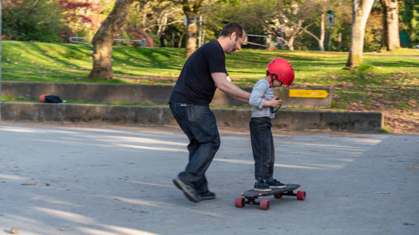 istock Father teaching his 7-years-old son how to ride an electrical skateboard. Stanley Park in Vancouver, Canada. The sunny warm spring day. 1146728730
