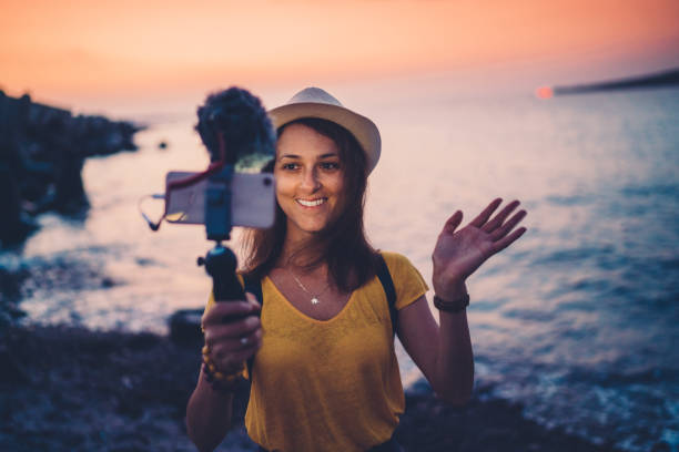 Young woman vlogging from beach holiday Young influencer vlogging from the seaside at sunset wonderlust stock pictures, royalty-free photos & images