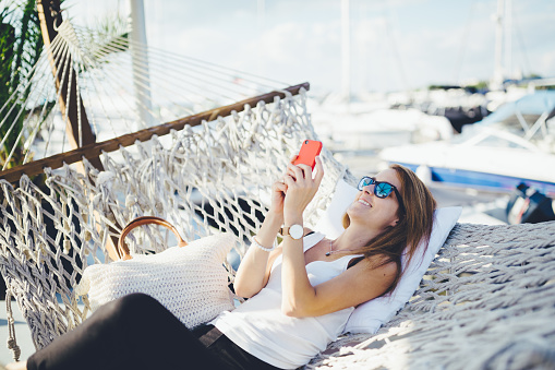 Relaxed woman in hammock using smartphone