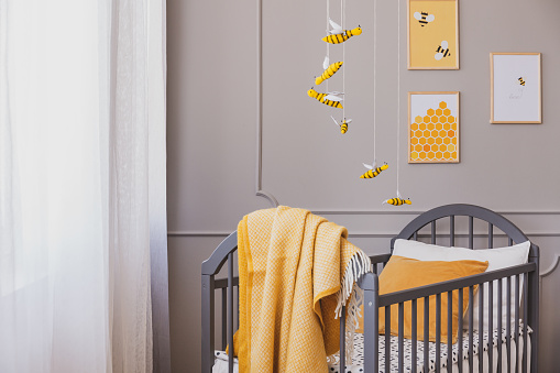 Yellow blanket on grey wooden crib in bright baby bedroom with yellow accents