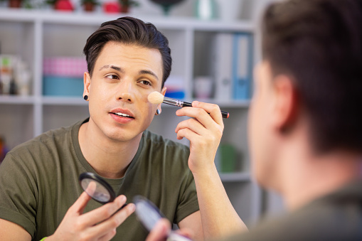 Guy applying makeup. Stylish good-looking man having neat haircut while getting ready and covering face in cosmetic