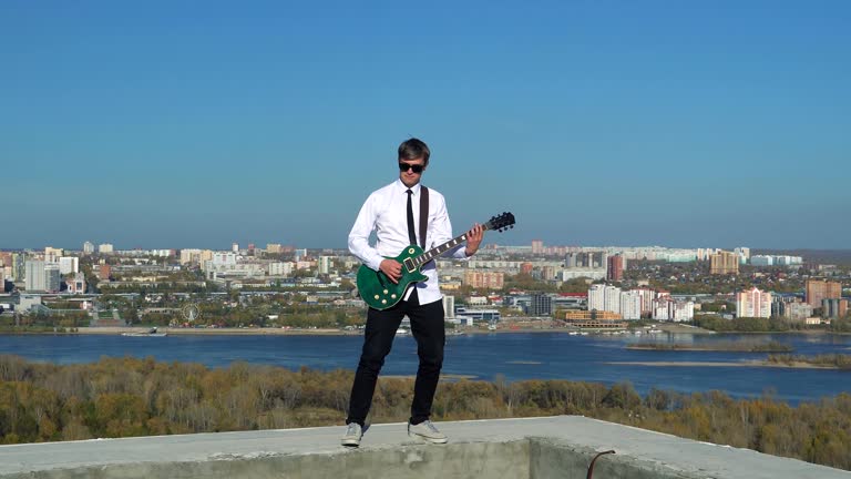 Young man playing guitar on against a blue sky. 4k