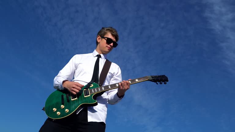 Young man playing guitar on against a blue sky. 4k