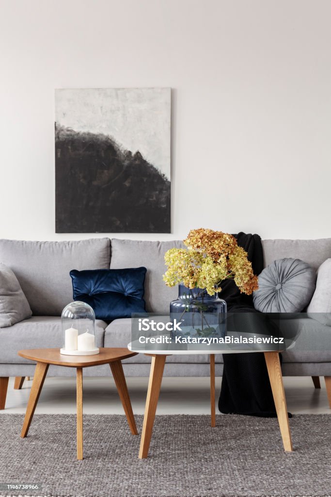 Blumen in blauer Glasvase und zwei weiße Kerzen auf Holzkaffechtischen in grauem, elegantem Wohnzimmer mit komfortablem Sofa - Lizenzfrei Grau Stock-Foto