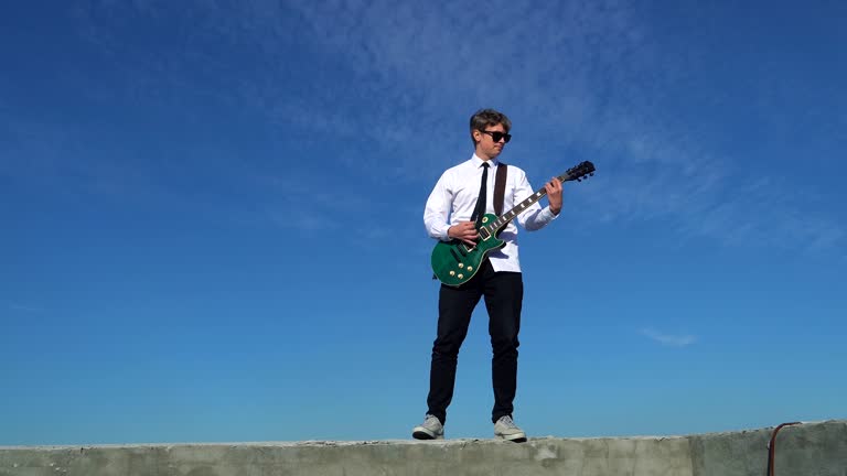 Young man playing guitar on against a blue sky. 4k