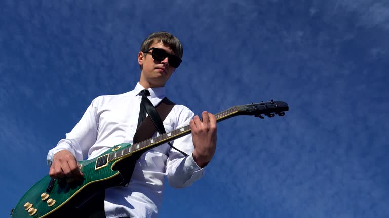 Young man playing guitar on against a blue sky. 4k