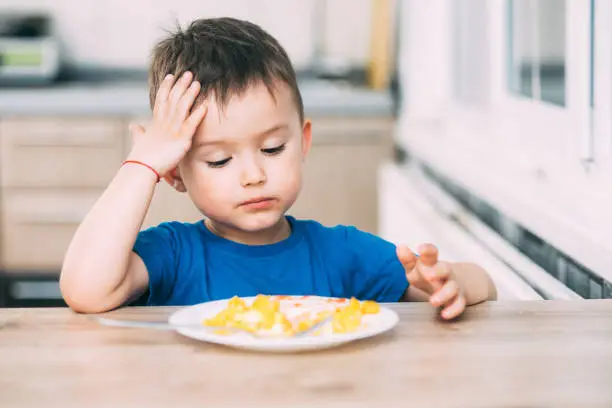 Photo of a child in a t-shirt in the kitchen eating an omelet, a fork