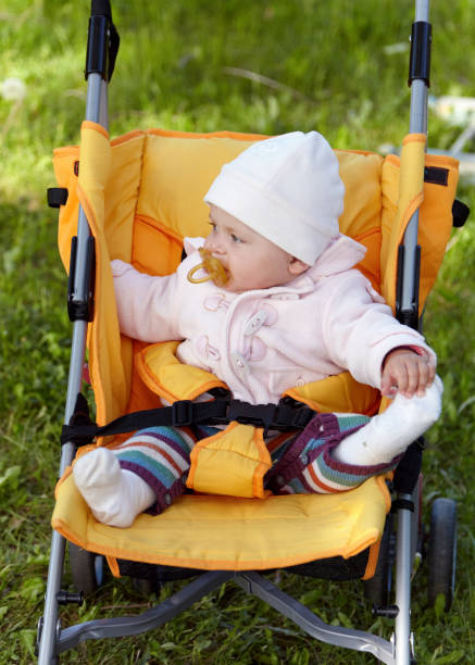 Pretty young woman walking through the public park with her baby son. He is in a baby carriage and this is their first walk.