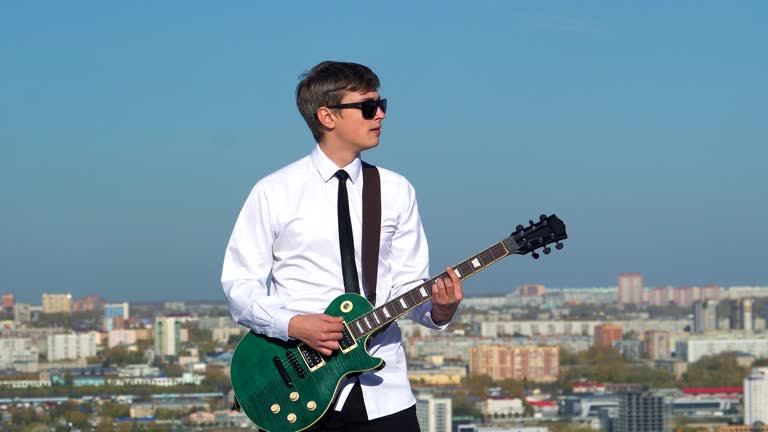 Young man playing guitar on against a blue sky. 4k