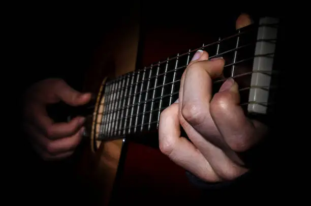 The image is low key the fingers of the musician playing on the frets of the guitar closeup.