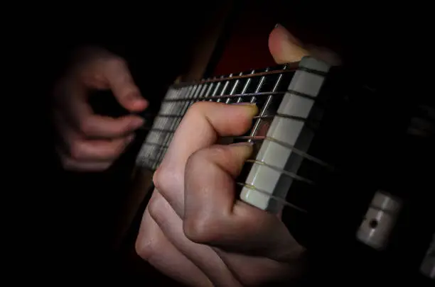 The image is low key the fingers of the musician playing on the frets of an acoustic guitar closeup.