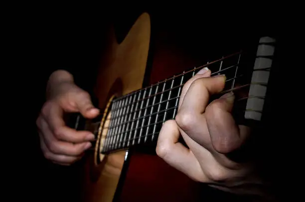 The image is low key the hands of a musician playing on the frets of the guitar closeup.