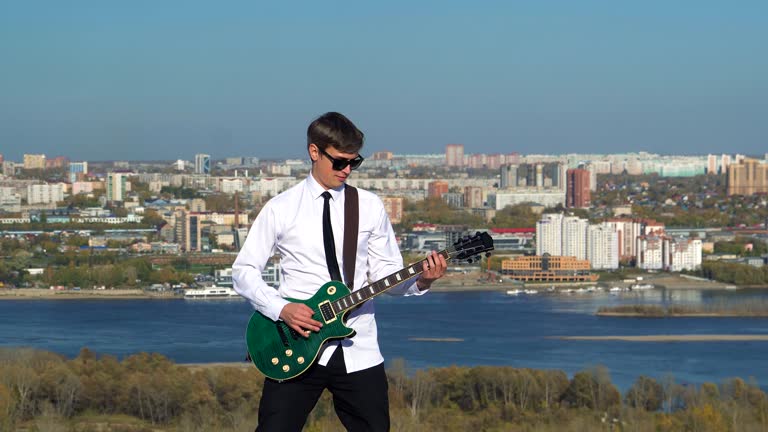 Young man playing guitar on against a blue sky. 4k