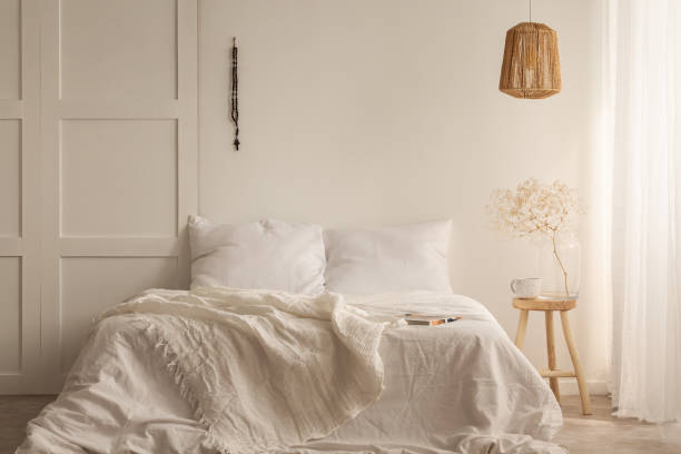 istock White king size bed with white bedding next to wooden table with white coffee mug and glass vase, rattan lamp above it, real photo 1146746193