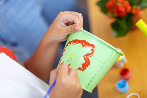 Painting cute flower. Close up of schoolboy painting cute flower on flowerpot at ecology lesson