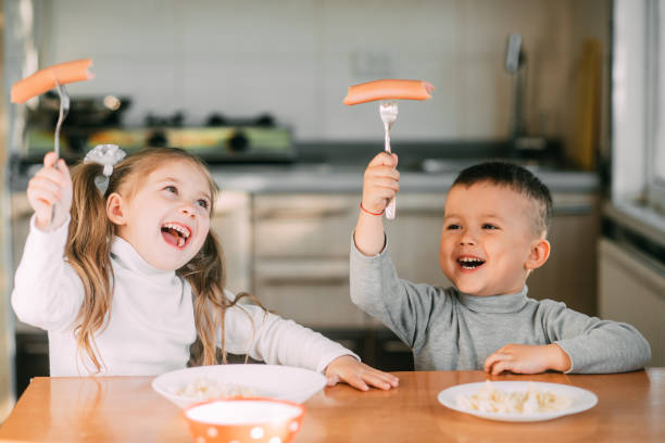 Boy and girl children in the kitchen eating sausages with pasta is very fun and friendly Boy and girl children in the kitchen eating sausages with pasta is very fun and friendly very sweet eating sausage stock pictures, royalty-free photos & images