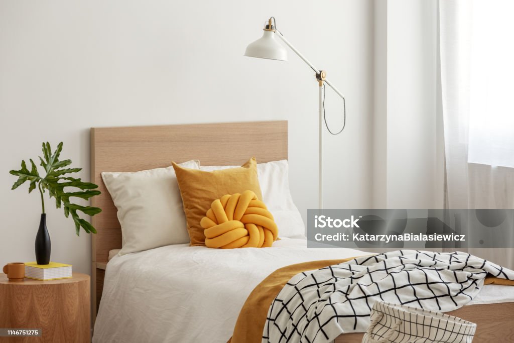 Yellow pillows and cozy blanket on single bed in elegant hotel room,green leaf in black vase on wooden bedside table Bed - Furniture Stock Photo