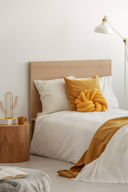 istock Yellow pillows and cozy blanket on single bed in elegant hotel room, copy space on empty white wall 1146751276