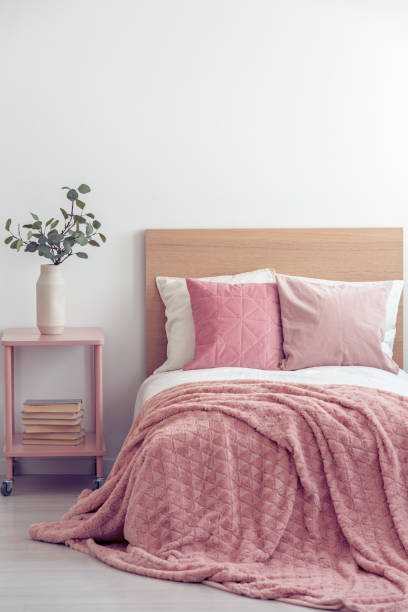 istock Pink pillows and cozy blanket on single bed in elegant hotel room, copy space on empty white wall 1146751279