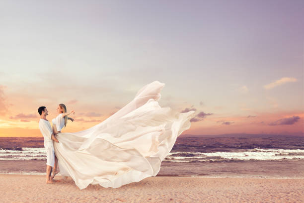 Happy couple embracing on the beach Happy couple embracing on the sea beach. Man holding woman in beautiful long dress on his hands honeymoon photos stock pictures, royalty-free photos & images