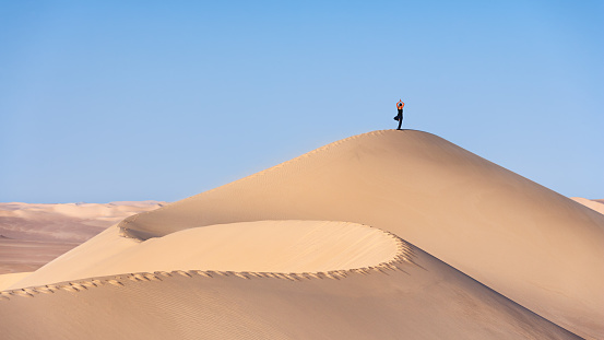 Young female practicing yoga on the top of sandune. The Sahara Desert is the world's largest hot desert with the biggest sand dunes.